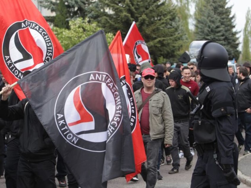 Participants in a demonstration carrying anti-fascist flags walk down a street in Troeglit