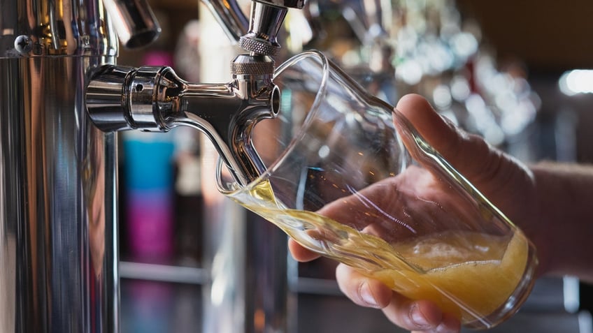 A hand holds a glass as cider is poured from a tap.