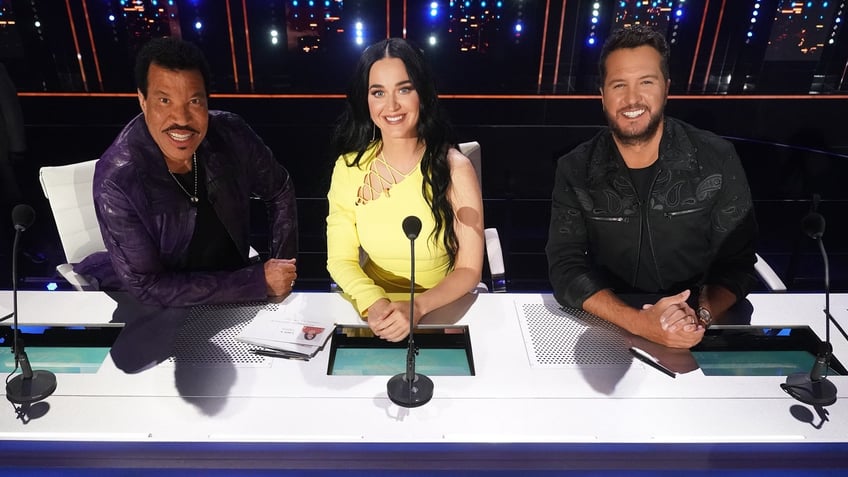 Lionel Richie in an all black outfit, Katy Perry in yellow dress, and Luke Bryan in an all black outfit at the judges table on "American Idol'