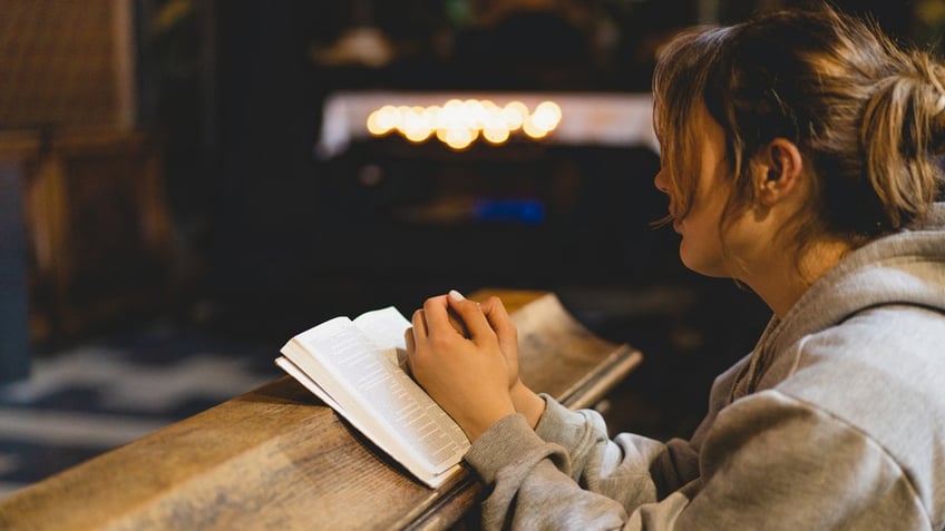 woman praying with bible in hands in church pew