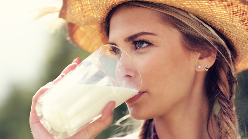 A woman wearing a straw hat drinks from a glass of milk.