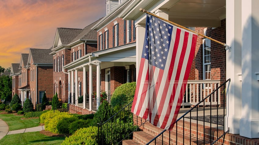 American Flags hang from the front of this traditional, brick homes in an All-American neighborhood. For Flag Day use