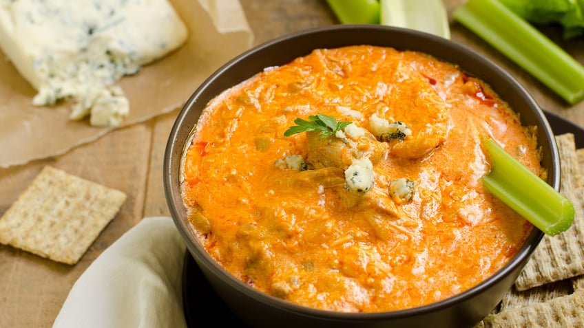 A bowl of Buffalo chicken dip with a stick of celery in it.