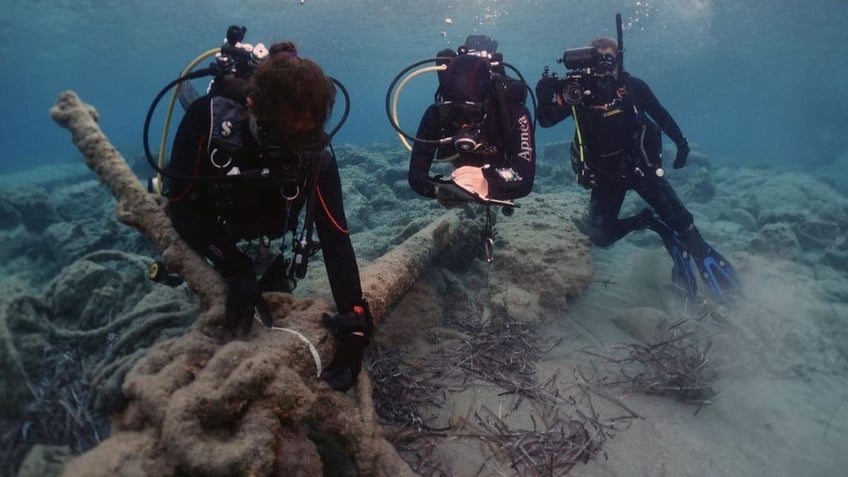 three divers exploring a piece of a ship on the sea floor