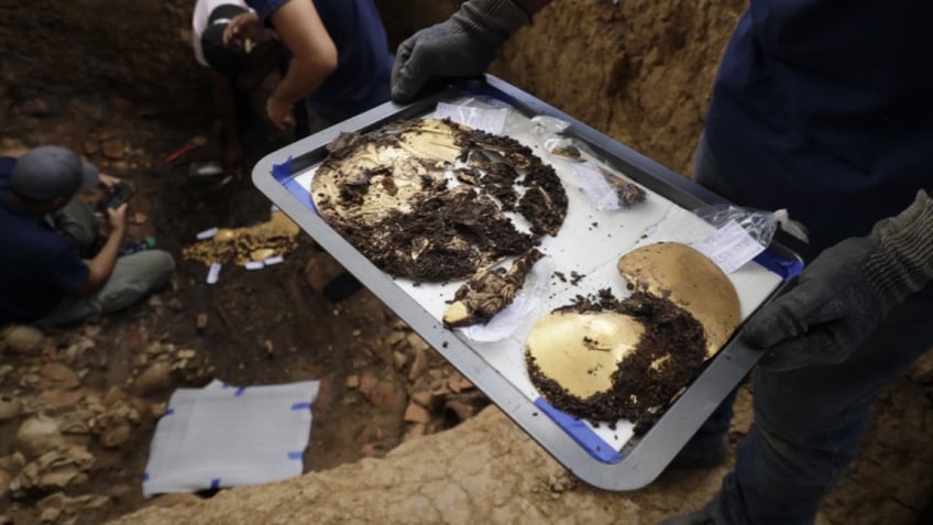 Archaeologist holding plate of gold items