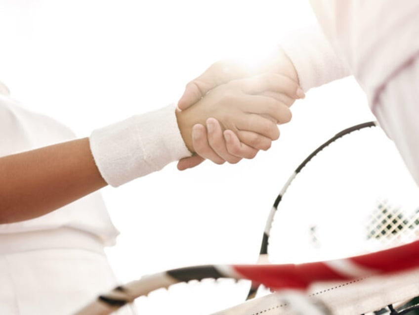 Shaking hands after good game. Close-up of man and woman in wristband shaking hands upon the tennis net