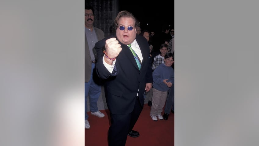 Chris Farley with his fist raised wearing a suit and sunglasses.