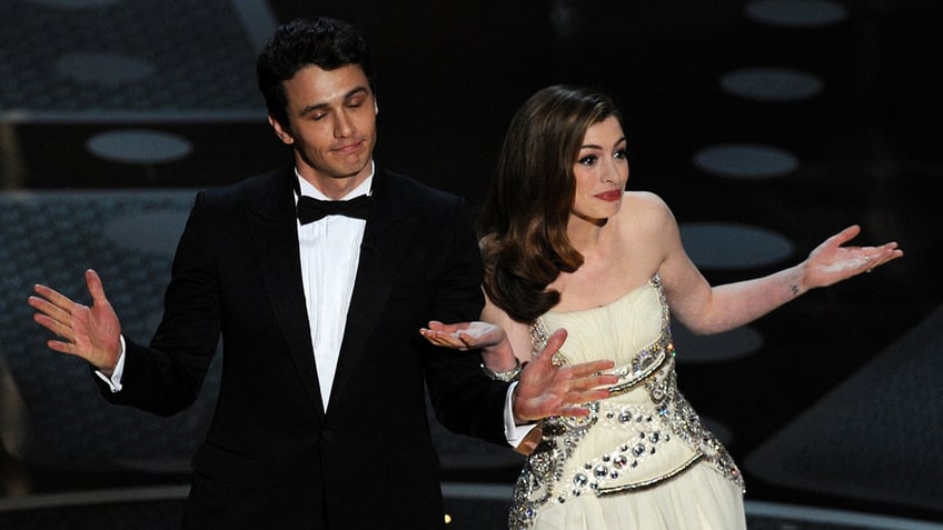 James Franco in a classic tuxedo and Anne Hathaway in a white strapless gown both shrug on the Oscars stage as hosts