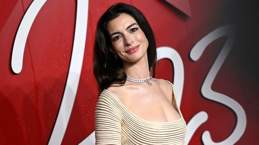 Anne Hathaway tilts her head back in a tan scoop short sleeve dress on the carpet
