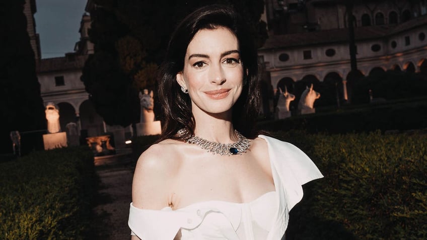 anne hathaway in white dress standing against background of chateau