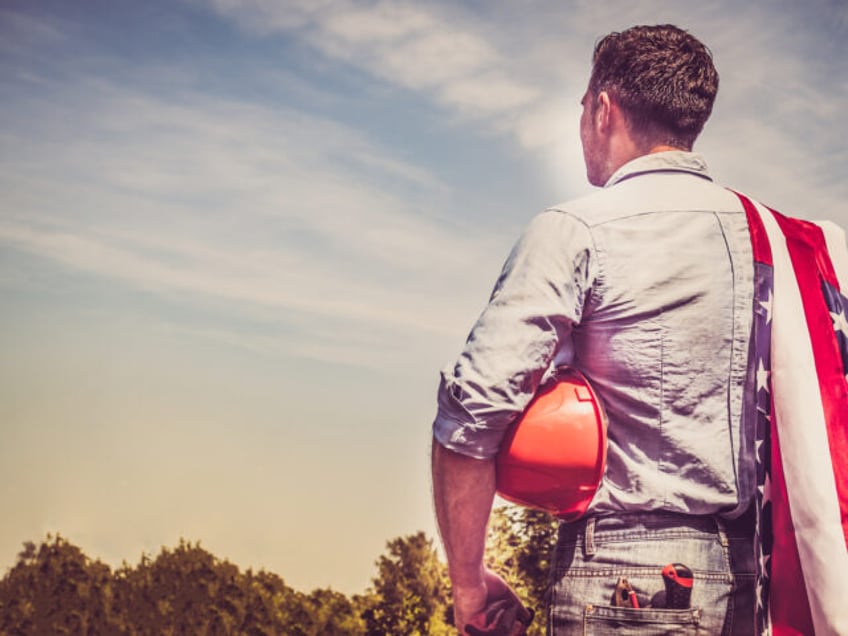 Attractive man in work clothes, holding tools and a US flag in his hands and looking into