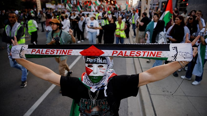 A demonstrator wearing a mask in the colors of the Palestinian flag holds up a scarf during a protest in support of Palestinians in Gaza