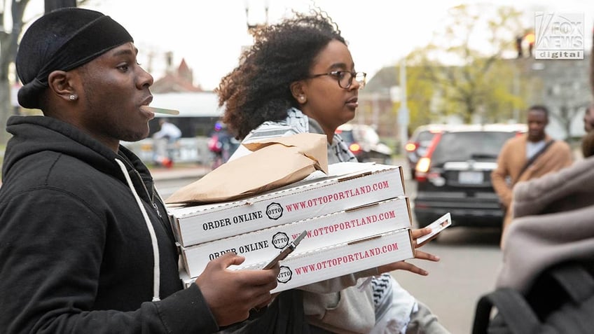 Students carrying boxes of pizza onto the campus.