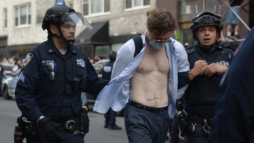 A man with an open shirt is arrested by police