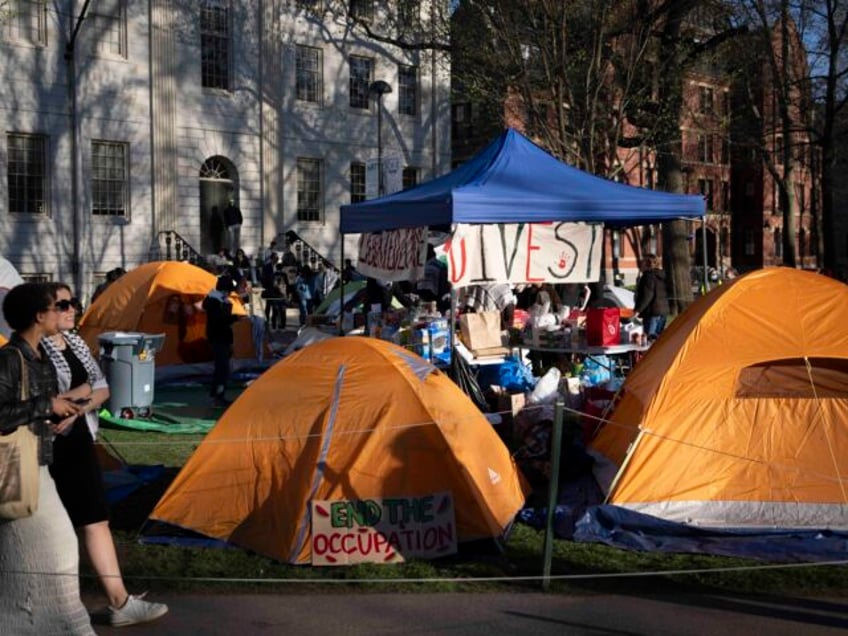 Passersby walk past tents at an encampment of students protesting against the war in Gaza,