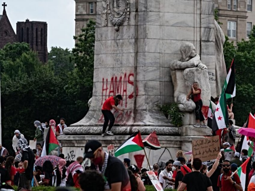 A person spray paints on the base of the Christopher Columbus Memorial Fountain as pro-Pal