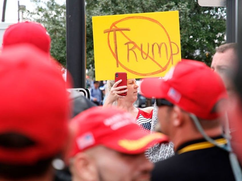 An anti-Trump demonstrator holds up a placard and films a group of supporters of US Presid