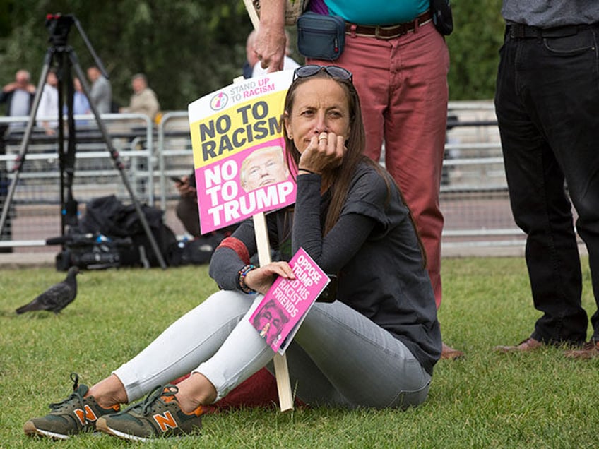 A woman sits with an anti-Trump placard during a protest against Donald Trump's visit to t