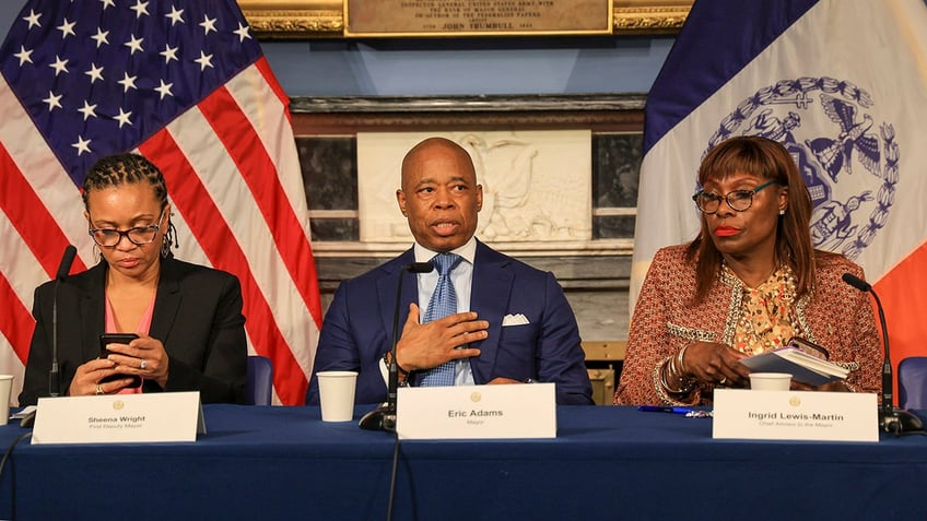 Adams at a news briefing flanked by other NYC officials at a table