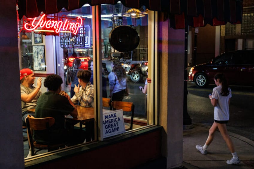 A group of three college boys wave a group of college girls walking past the restaurant lo