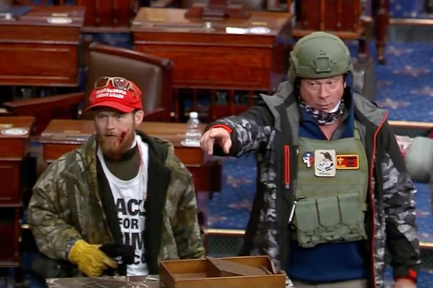 This image from Senate Television video, contained in the Justice Department's affidavit in support of a criminal complaint and arrest warrant for Larry Rendall Brock, shows Brock, right, on the floor of the Senate at the U.S. Capitol on Jan. 6, 2021, in Washington. A federal appeals court in Washington, on March 1, 2024, has ordered a new sentence for Brock, who stormed the U.S. Capitol dressed in combat gear, in a ruling that could impact dozens of other cases stemming from the Jan. 6, 2021, attack. While a panel of the U.S. Court of Appeals for the D.C. Circuit upheld Brock's conviction, the court said a judge wrongly applied an enhancement that lengthened the recommended prison sentence range under federal guidelines. (Department of Justice via AP)