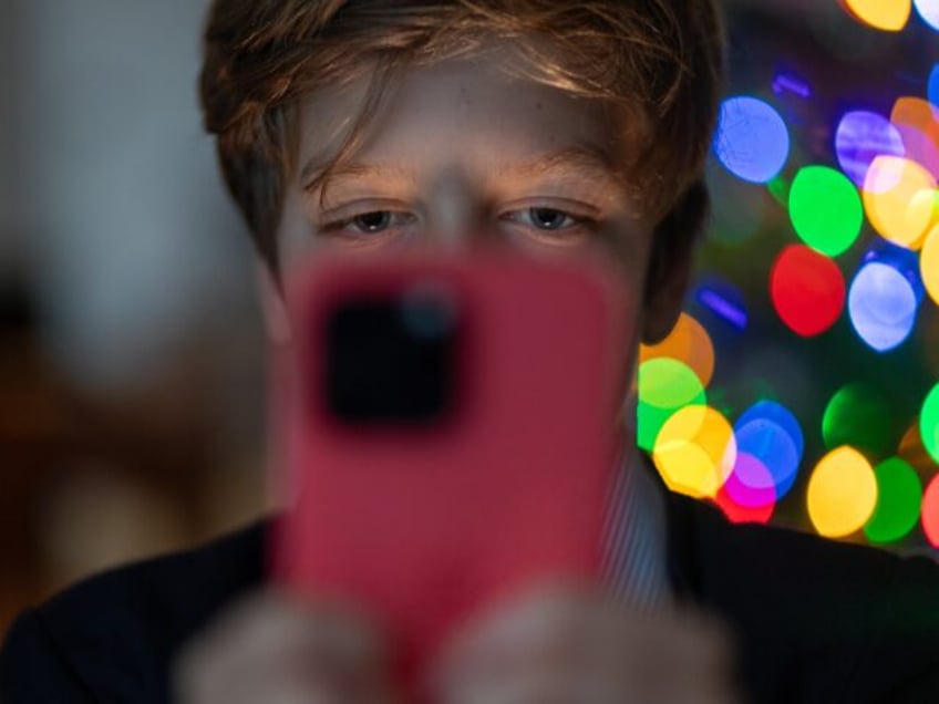 BATH, UNITED KINGDOM - DECEMBER 19: A 12-year-old boy looks at an iPhone screen on December 19, 2023 in Bath, England. The amount of time children spend on screens each day rocketed during the Covid pandemic by more than 50 per cent, the equivalent of an extra hour and twenty …