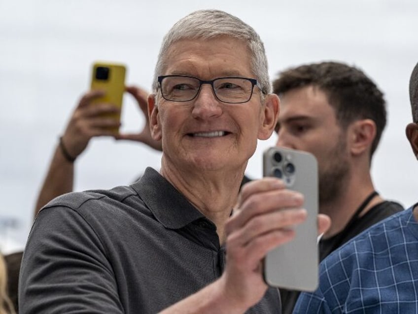 Tim Cook holds an iphone with a grin