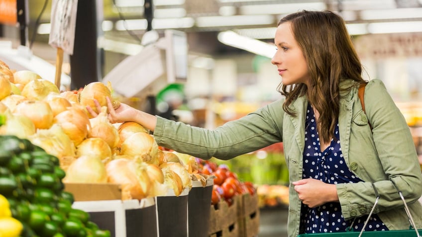 A woman inspects an onion while shopping.