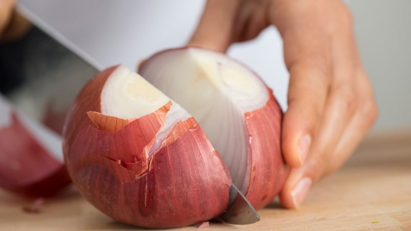 A knife cuts into an onion.