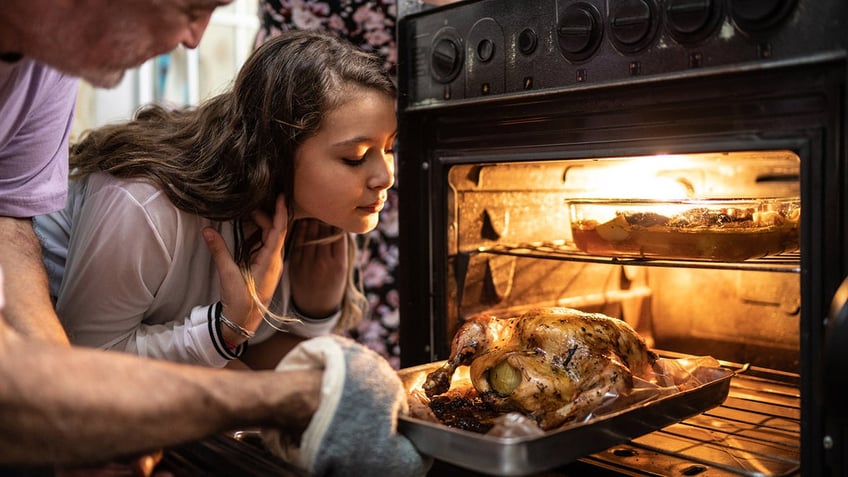 Grandfather and young girl taking a cooked turkey out of the oven.