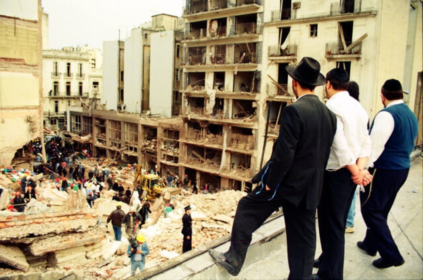 Jewish men, right, look on as rescuers sift through the rubble at the site of a car-bombin