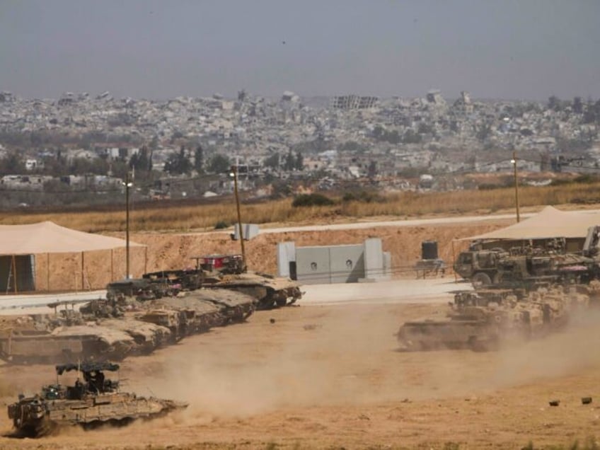 Israeli soldiers work on tanks and armored vehicles at a staging area near the border with