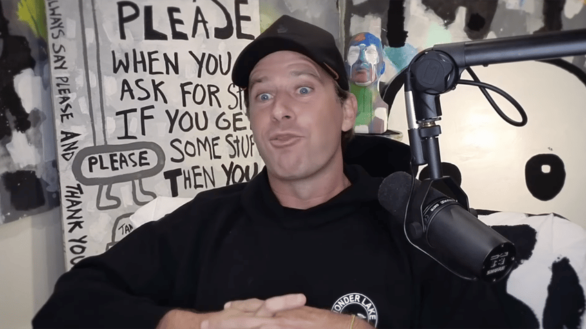 Armie Hammer in a black sweatshirt and black hat speaks on a podcast looking animated