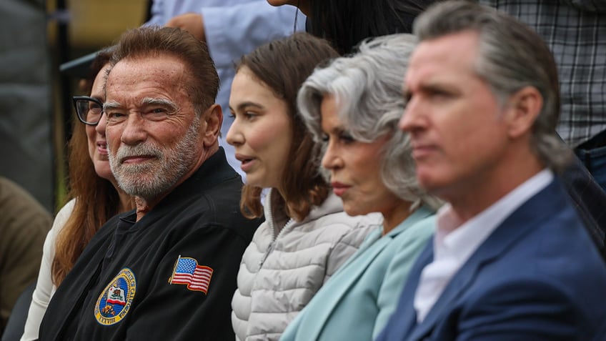 Arnold Schwarzenegger in focus sits next to a woman, then Jane Fonda and Governor Gavin Newsom at an event for the environment in Los Angeles