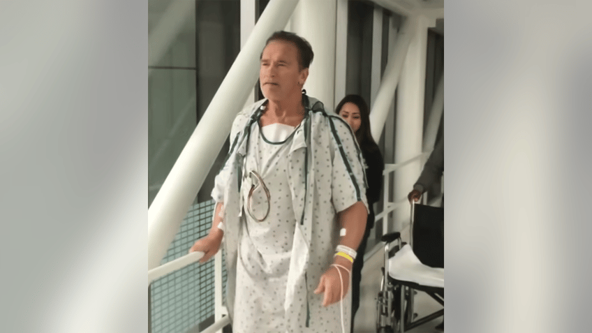 Arnold Schwarzenegger in a hospital gown walking around the hospital