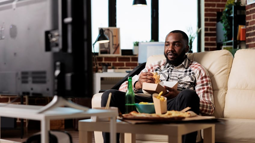 man eating fast food at home, watching television