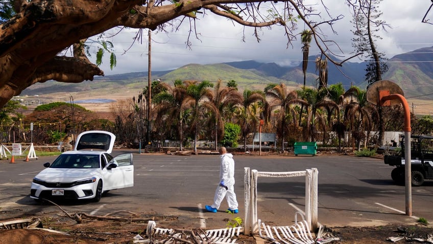 The Rev. Ai Hironaka, resident minister of the Lahaina Hongwanji Mission, walks in the parking lot wearing a protective white suit as he visits his temple and residence destroyed by wildfire