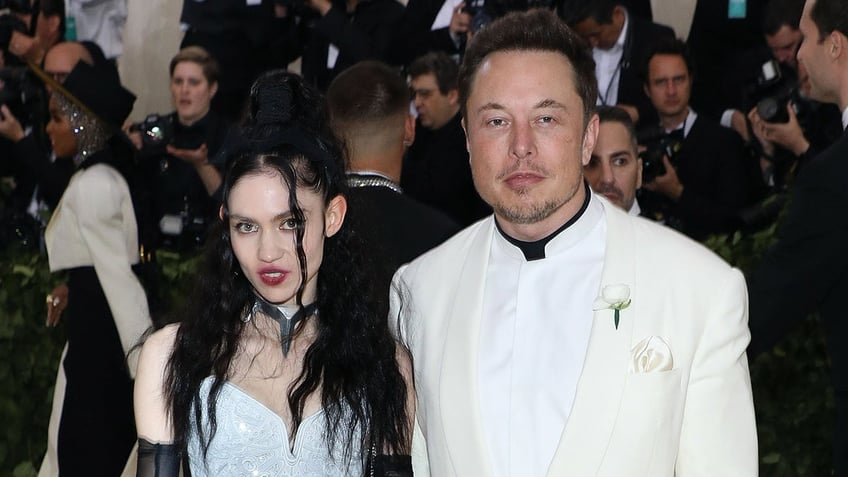 Elon Musk in a white tuxedo and Grimes in a white dress and black accents on the Met Gala red carpet