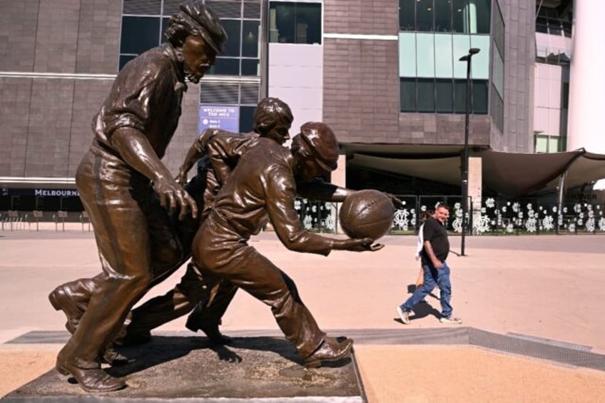 A man looks at a sculpture of Australian Rules footballers outside the Melbourne Cricket G