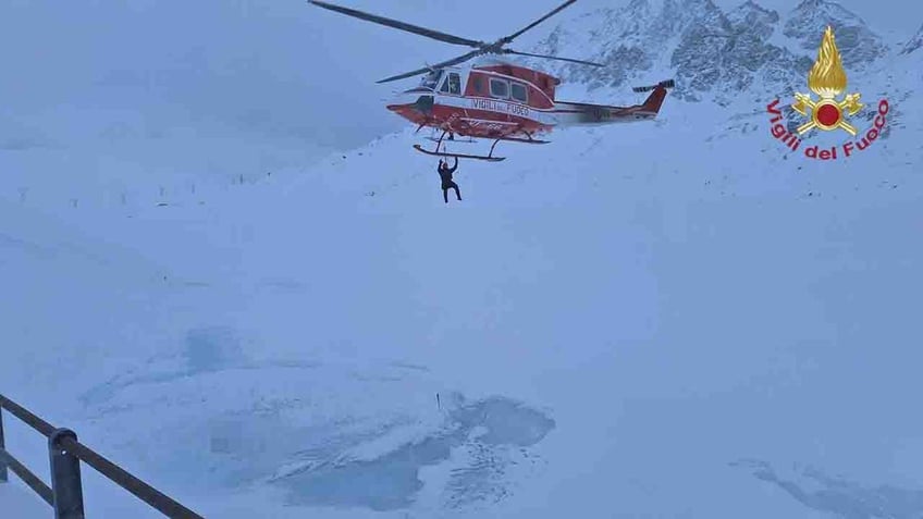 helicopter lowers rescuer over lake in Alps