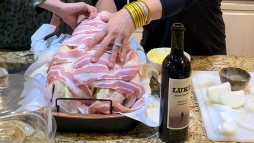 Two sets of hands wrapping a turkey in bacon and a pillowcase.