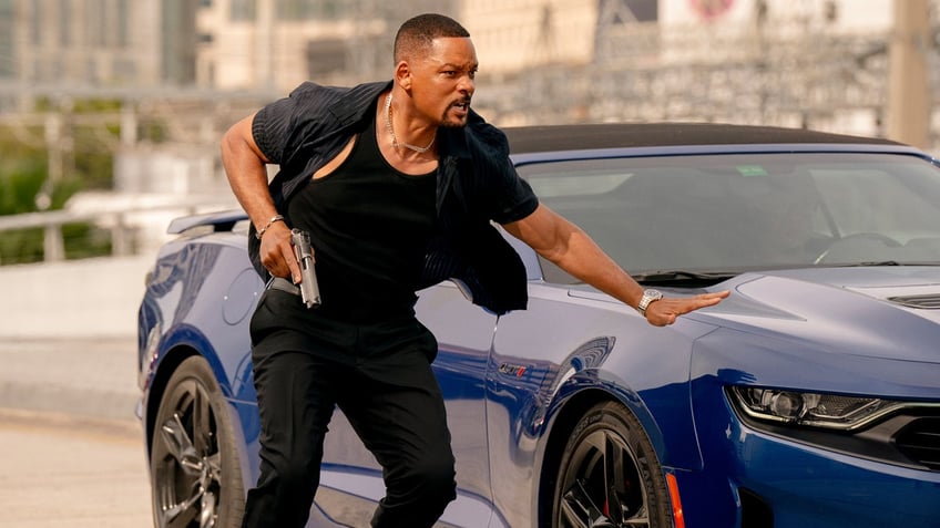 Will Smith holds a gun next to a blue sports car in a still from "Bad Boys: Ride or Die."