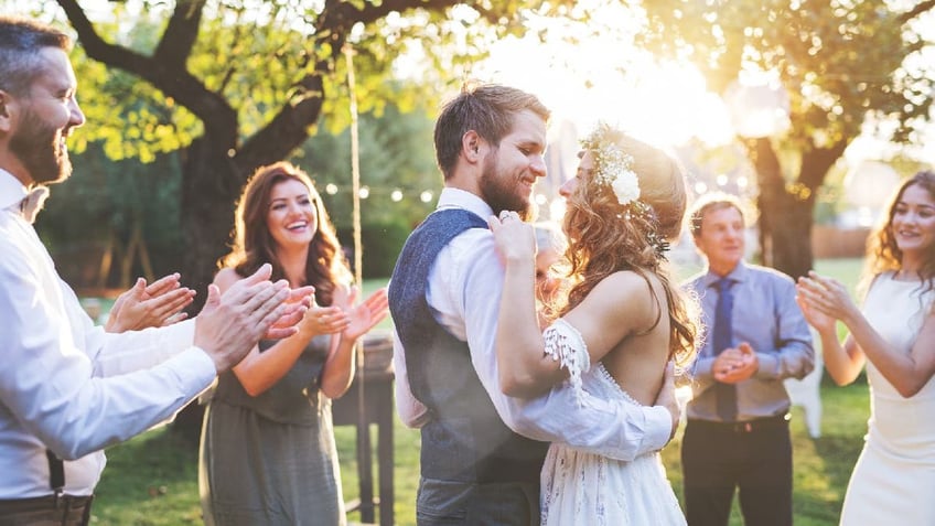 Wedding reception outside in the backyard. Bride and groom with a family dancing.