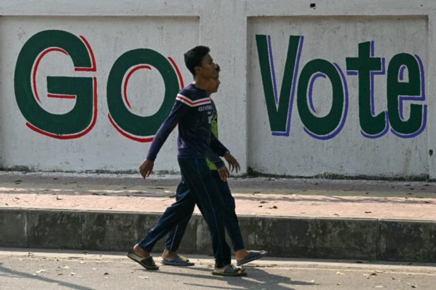 Men walk past a wall writing urging people to vote in Dhaka on January 6, 2024, on the eve of Bangladesh's general election