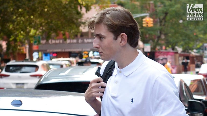 Barron Trump wears a white polo shirt, black jeans and Adidas sneakers as he leaves college with a black backpack on his shoulder