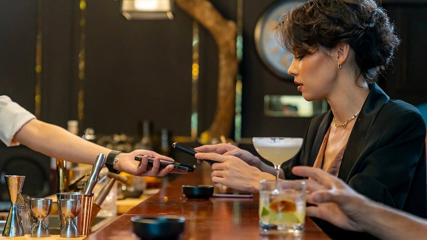 A woman uses her phone to make a payment at a bar.