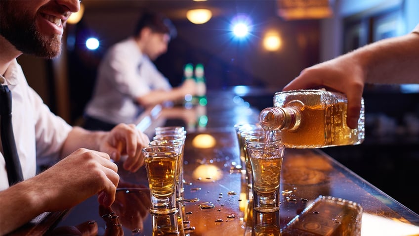 Bartender pouring shots of liquor as customer sits across smiling