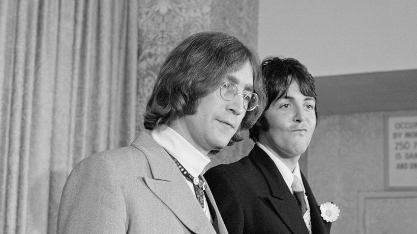 John Lennon and Paul McCartney looking to the side and standing next to each other.