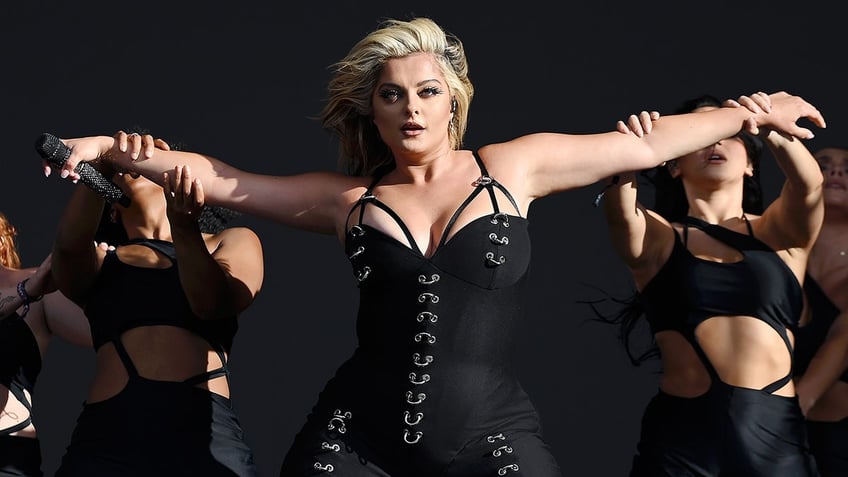 Bebe Rexha in a black corset with straps outstretches her arms on stage