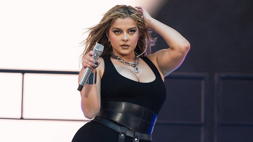 Bebe Rexha holds her microphone on stage as she performs on stage in a black outfit at Coachella